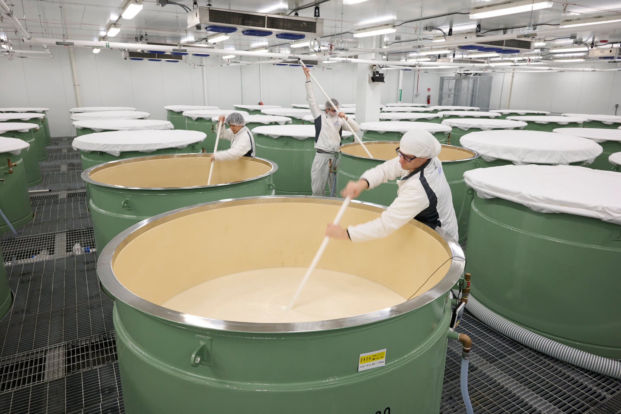 Three brewers stirring fermentation tanks