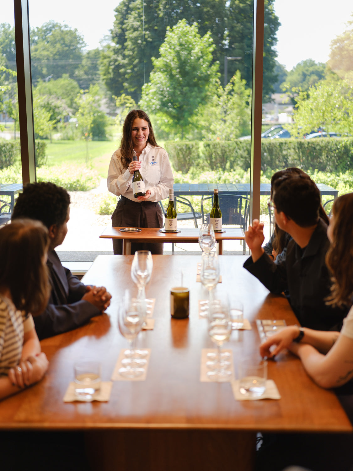 Woman presenting sake at a table with participants in the Tasting Room