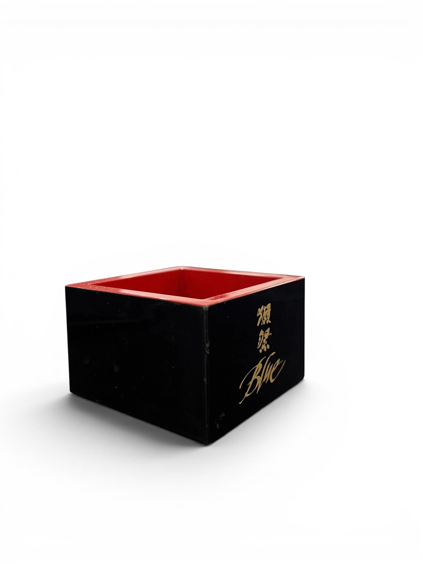 Dassai Blue traditional wooden Masu cup in black with a red interior and gold logo branding.