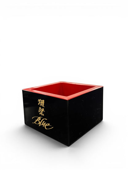 Dassai Blue traditional wooden Masu cup with a black exterior, red interior, and gold logo branding.
